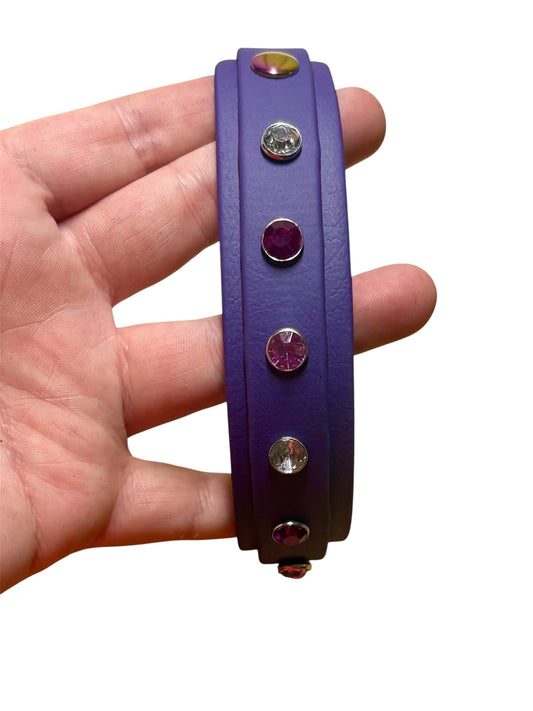 Purple biothane dog collar with gemstone accents held in a hand on a white background